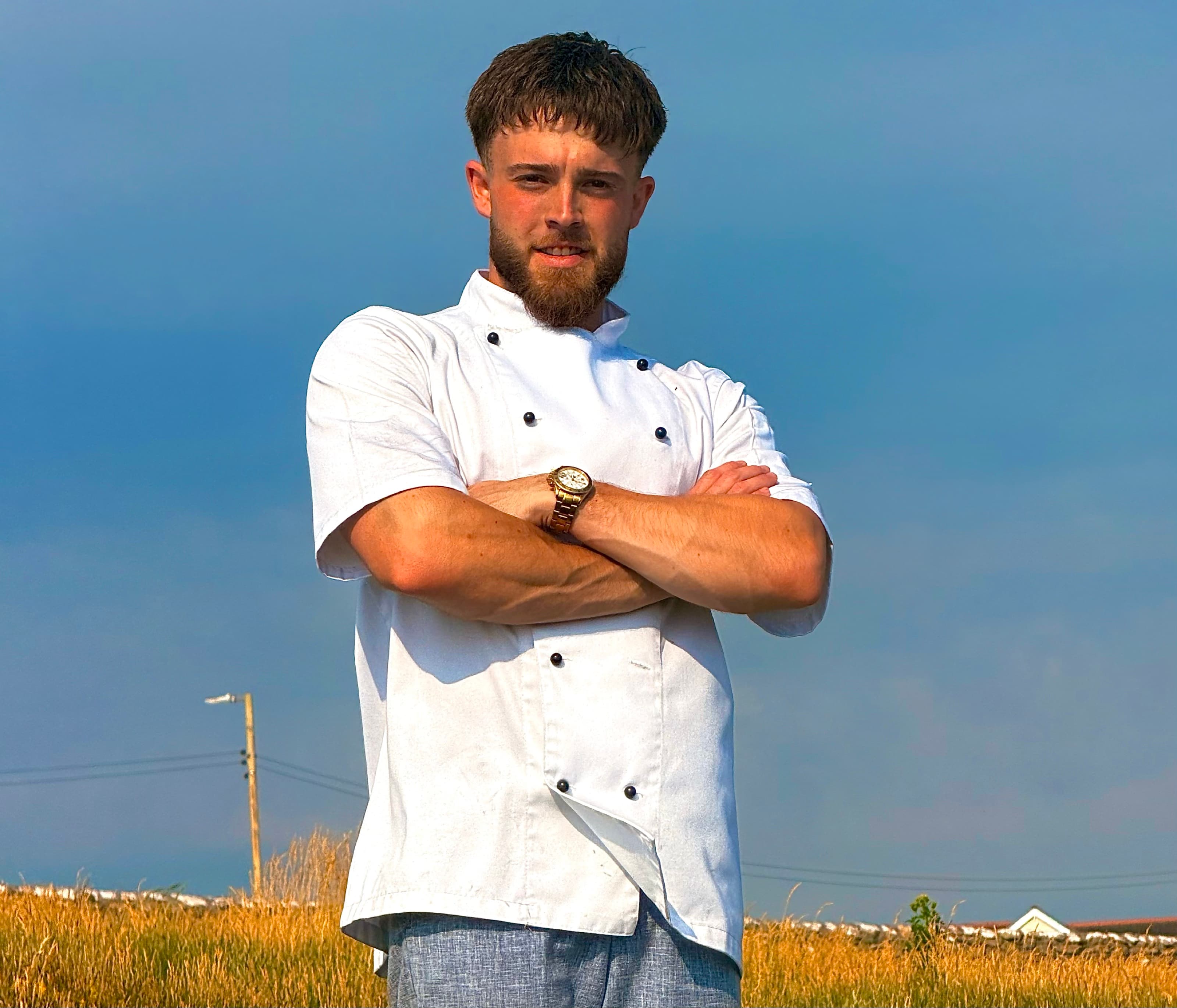 Samuel in chef’s whites, arms crossed, in a Somerset field